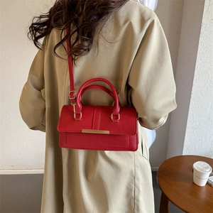 Elegant red leather handbag with gold metal clasp shown on model in a stylish indoor setting