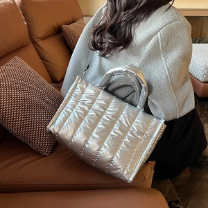 Silver quilted puffer handbag with metallic finish and detachable strap on leather sofa