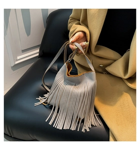 Detail of light gray bucket bag featuring long leather tassels and a bright yellow lining