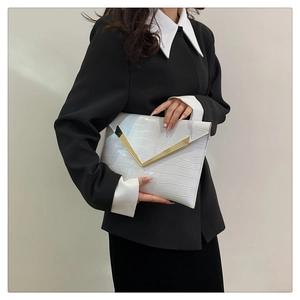 Detail of white crocodile embossed envelope clutch bag with gold V-shape metal hardware