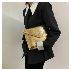 Detail of a gold crocodile embossed envelope clutch with a metal V-shaped trim detail
