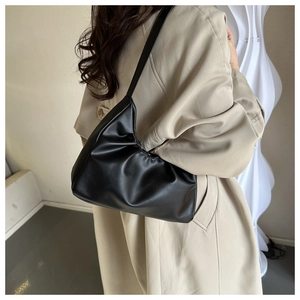 Model wearing a black pleated faux leather shoulder bag with a minimalist half-moon design