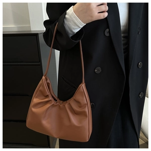 Detail view of brown pleated crescent shoulder bag worn with a black blazer