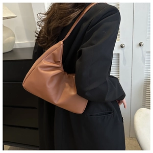 Detail of a brown pleated PU leather underarm bag worn with a black blazer