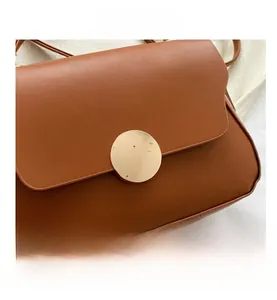 Detail of caramel brown leather handbag with a wavy flap and gold circular buckle
