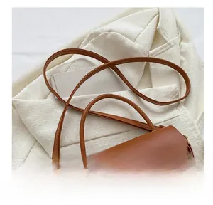 Detail view of brown leather crossbody bag with round metal buckle on white blazer