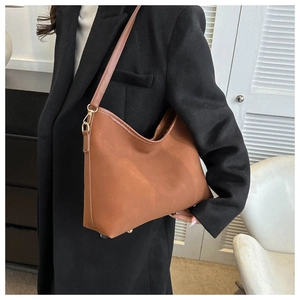 Detail of a brown suede hobo bag with gold hardware worn on the shoulder in a home setting