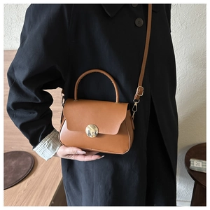 Close-up of brown leather box bag with golden metal hardware and top handle for women