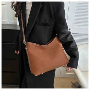 Detail of caramel brown leather tote bag with gold metal buckles on minimalist shoulder strap