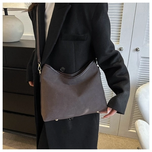Detail of dark brown tote bag with matte texture and gold hardware on a black wool coat