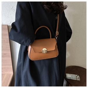 Detail of a brown leather shoulder bag with circular gold metal clasp and matte texture
