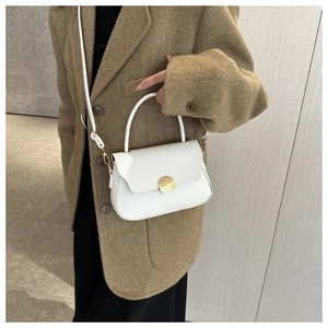 Close-up of a white box bag with large gold magnetic buckle on a brown blazer outfit