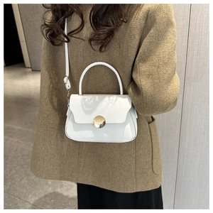 White vintage box bag with gold buckle shown on shoulder of model in brown coat