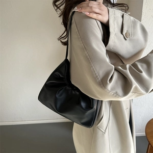 Minimalist black leather underarm bag for women shown with a casual beige coat