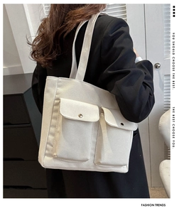 Detailed back view of a large cream canvas tote bag with two front pockets on a model