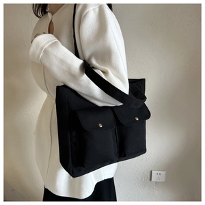 Detail of black canvas tote bag featuring dual front pockets with metal snap buttons