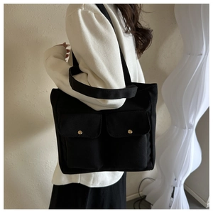 Detail of black canvas tote bag with front flap pockets and gold metal buckles worn by model