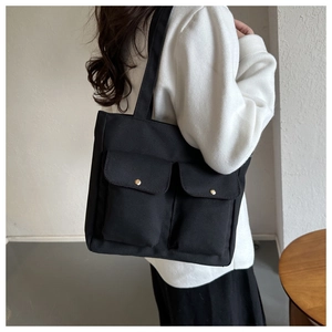 Detail of black canvas tote bag showing front flap pockets with gold snap buttons
