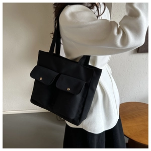 Detail of black canvas tote bag showing double front pockets with gold metal buttons