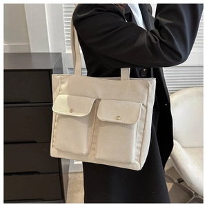 Detail of off-white canvas tote bag featuring double front pockets with metal snap buttons