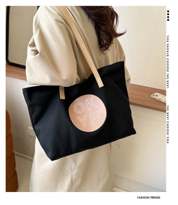 Close-up of black canvas tote bag with beige leather strap and circular OKYF logo detail