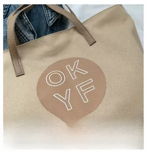 Detail of khaki canvas tote bag featuring OKYF logo print and premium leather handles