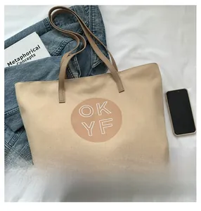 Detailed top view of a large beige canvas tote bag with OKYF logo on a white fabric background