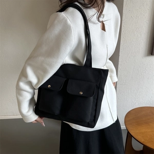 Black canvas tote bag with dual front pockets and gold buckles shown on shoulder