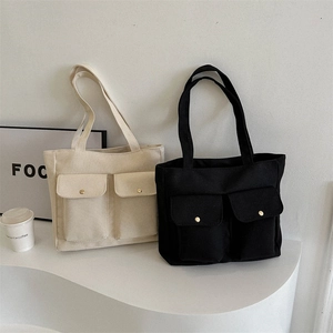 Large canvas tote bag with front flap pockets available in black and off-white colors