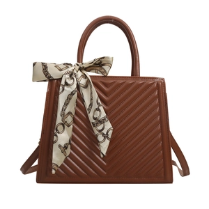 Brown V-quilted tote bag with silk scarf accessory on a minimalist white background