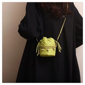Close-up of green quilted bucket bag with gold chain strap and heart charms