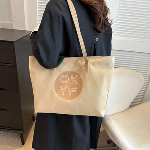Chic beige canvas tote bag with 'OK YF' print and leather straps shown on a model