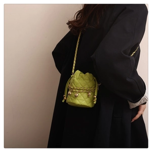 Lime green quilted mini bucket bag with gold chain strap and heart charms worn on a coat