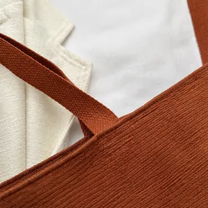 Detalle de bolso tote de pana marrón que muestra la textura de rayas y costuras del asa