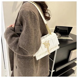 Detail of white quilted crossbody bag featuring golden VS logo and fringe pendant