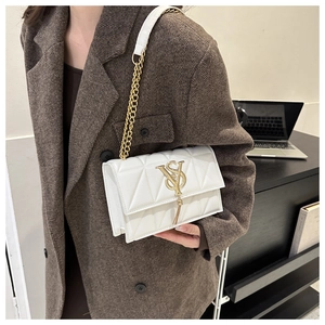 Detail of ivory quilted crossbody bag with gold VS logo and fringe on wool coat