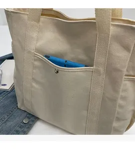 Gros plan d'un sac cabas en toile crème montrant la poche avant et les coutures soignées