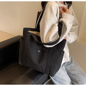 Détail d'un sac fourre-tout noir en toile avec poches latérales et anse en sangle sur modèle