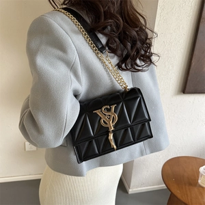 Retro black quilted crossbody bag with gold VS clasp and tassel, worn by a model