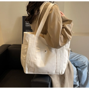 Détail d'un grand sac cabas en toile beige porté par un mannequin en style décontracté