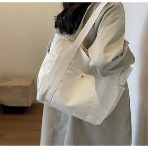 Vue latérale du sac fourre-tout en toile crème avec bandoulière large et poche latérale