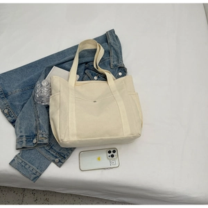 Vue à plat du fourre-tout en toile blanc cassé avec poches et accessoires mode