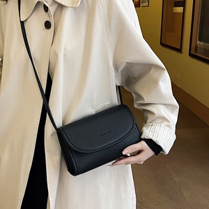 Minimalist black lychee texture crossbody bag with adjustable strap worn on beige coat