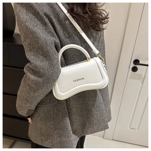 Sac à main blanc en cuir avec base incurvée porté sur une veste de costume grise
