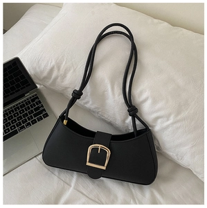 Detail of black baguette bag with gold horseshoe buckle and knotted strap on white bedding