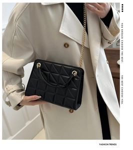 Detail of black quilted shoulder bag with gold chain strap shown on beige coat