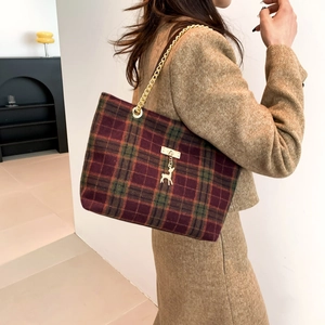 Plaid tote bag with gold chain strap and deer charm shown in a cozy indoor setting