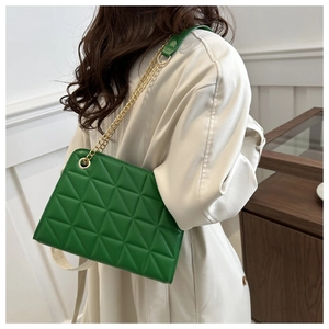 Detail of green quilted crossbody bag with golden chain strap on a model's shoulder
