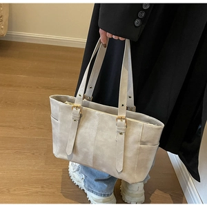 Detail of grey commute tote bag with gold metal buckles and side pocket on wooden floor