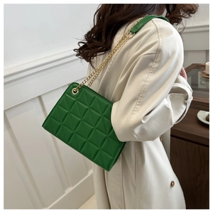 Detail shot of a green quilted shoulder bag with golden chain straps on a model